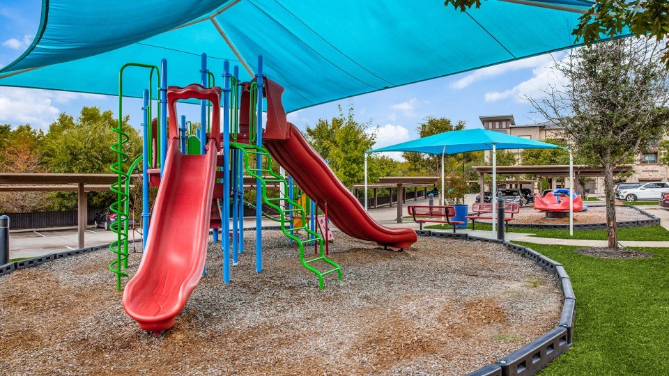 a playground with a blue canopy and slides at The Twin Creeks Crossing
